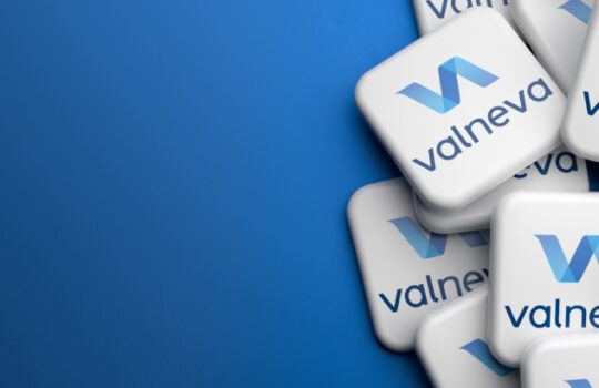 Logos of the French biotechnology company Valneva on a heap on a table. Copy space. Web banner format.