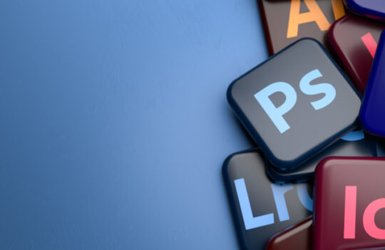 Logos of the major parts of the Creative Cloud Apps Suite (Illustrator, Photoshop, InDesign, Lightroom Classic, Premiere Pro) on a heap on a table. Copy space. Web banner format.