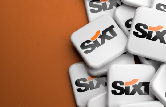 Logos of the German rental car company Sixt on a heap on a table. Copy space. Web banner format.