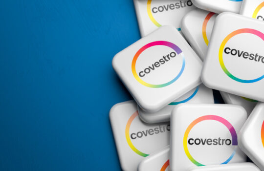 Logos of the German producer of polyurethane and polycarbonate Covestro on a heap on a table. Copy space. Web banner format.