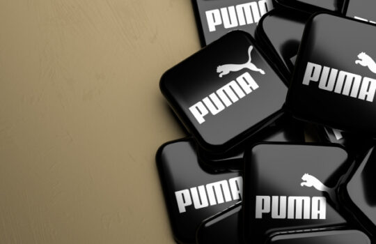 Logos of the German sportswear and apparel company Puma SE on a heap on a table. Copy space. Web banner format.
