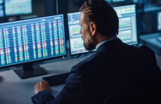 Professional Financial Data Analysts Working in a Modern Monitoring Office with Live Analytics Feed on a Big Digital Screen. Monitoring Room with Finance Specialists Sit in Front of Computers.