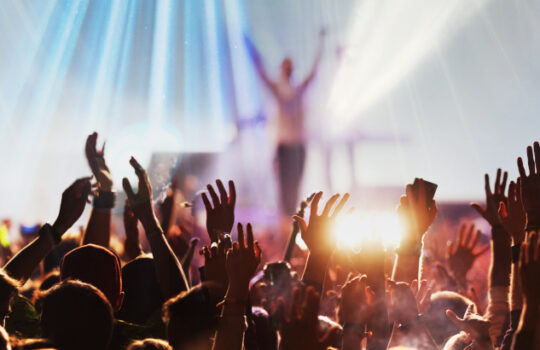 CTS Eventim Aktie: crowd with raised hands at concert festival banner