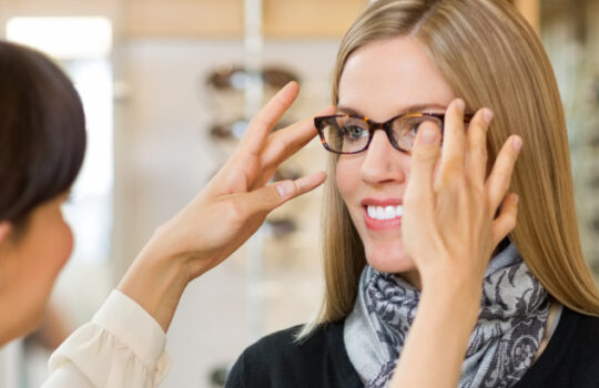 Fielmann Optiker Young salesgirl assisting female customer to in wearing glasses at shop