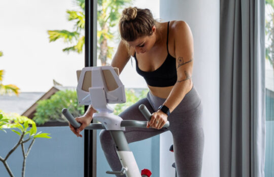 Peloton Aktie – Woman exercising on stationary bike at home