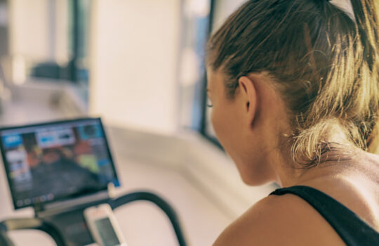 Smart fitness home workout biking screen with online classes woman training on stationary bike equipment indoors for biking exercise. Indoor cycling. Focus on the sweat on person's back.