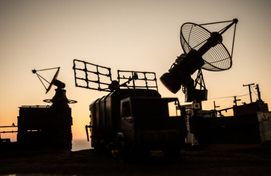 Creative artwork decoration. Silhouette of mobile air defence truck with radar antenna during sunset. Satellite dishes or radio antennas against evening sky. Selective focus