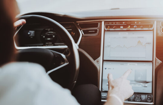 Caucasian Man In The Tesla Car. Front Seat Concept. Innovation Technology. New Generation Electro Hybrid Vehicle. Luxury Design. Futuristic Power. Hands On Display. Behind The Wheel.