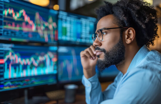 A side view of a trader analyst at the desktop, analyzing financial chart, stock quotes, share prices, trading online, checking data on cryptocurrency graph on computer screen, making notes