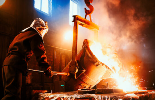 Workers operates at the metallurgical plant. The liquid metal is poured into molds. Worker controlling metal melting in furnaces.