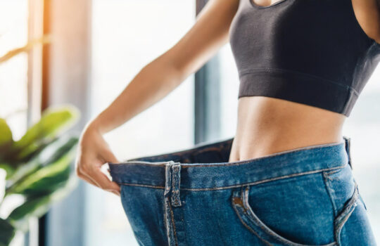 Slim woman celebrates weight loss, wearing oversized pants, symbolizing success and transformation