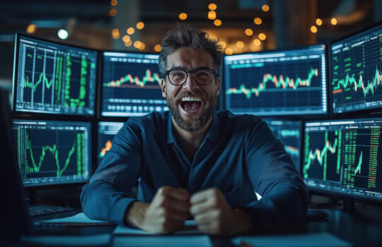Excited trader celebrating success in front of multiple computer screens showing stock market charts