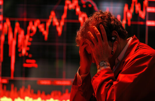 Stressed man in red jacket facing stock market crash. Stock trader with head in hands as charts on screens show severe market downturn. --ar 16:9 --stylize 250 --v 6 Job ID: 62301880-4ffd-44e3-bb23-631345424a89