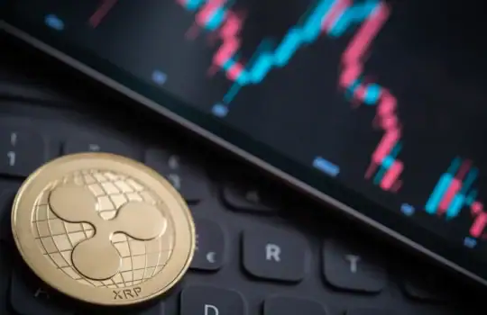 Ripple XRP Coin auf Laptop mit Kursdiagramm im Hintergrund.