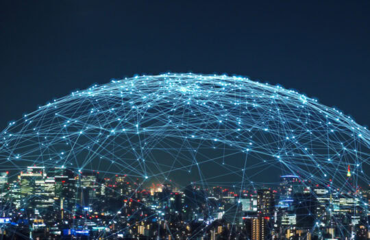 Night city skyline with a glowing blue network of interconnected lines forming a dome overhead, illustrating connectivity at night.