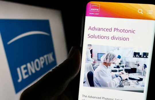 Smartphone screen shows a page titled 'Advanced Photonic Solutions division' with a lab technician at work in a cleanroom image.