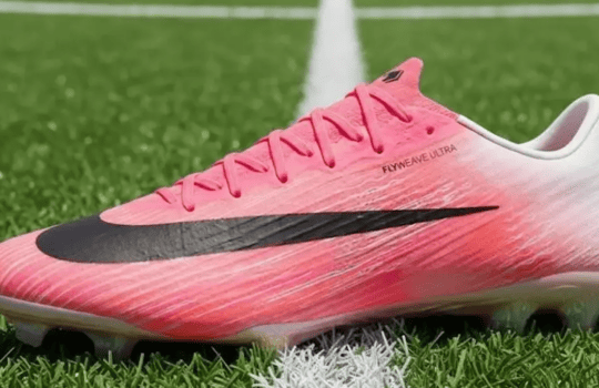 Pink Nike Flyknit Ultra soccer cleat with black swoosh on a turf field.