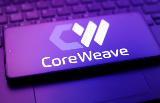 Phone lying on a laptop with a purple glow, showing the CoreWeave logo on the screen.