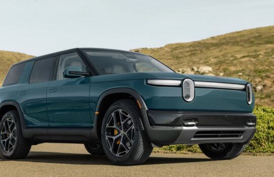 Teal-blue SUV shown from the front-left, parked on a paved road with grassy hills in the background.