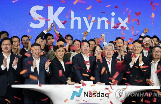 Group of SK hynix executives and staff celebrating a Nasdaq listing, raising hands with orange confetti against a blue backdrop that reads 'SK hynix'.