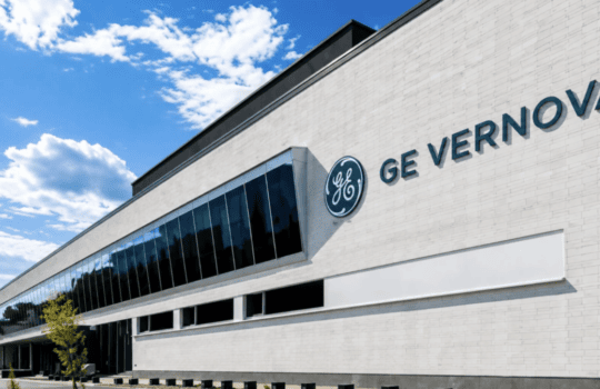 Exterior of GE Vernova corporate building with a glass facade and blue sky above, GE logo visible on the wall
