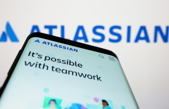 Phone screen shows Atlassian branding and the slogan 'It's possible with teamwork' with a blurred blue Atlassian logo in the background.