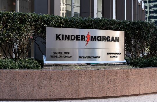 Kinder Morgan sign with red lightning bolt logo on stainless plaque in a landscaped plaza outside a modern office building