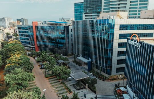 Aerial view of a modern corporate campus with glass-front towers and a tree-lined central plaza.