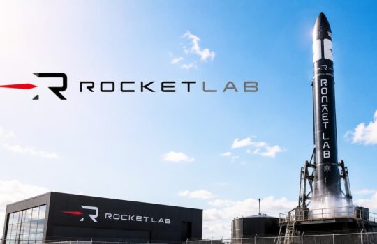 Rocket Lab logo on a building with a tall rocket on a launch pad against a blue sky. Quiet, sunny day at the launch site.