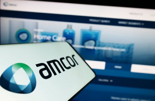 Close-up of a smartphone screen displaying the Amcor logo with a blurred blue product-site header in the background.