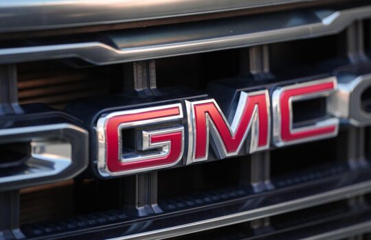 Close-up of the GMC emblem in red and chrome on a vehicle grille.