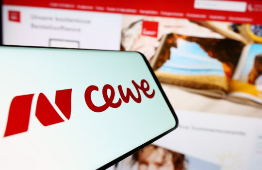 Close-up of a light-blue surface displaying bold red cursive letters, with a blurred computer screen showing a red header in the background.