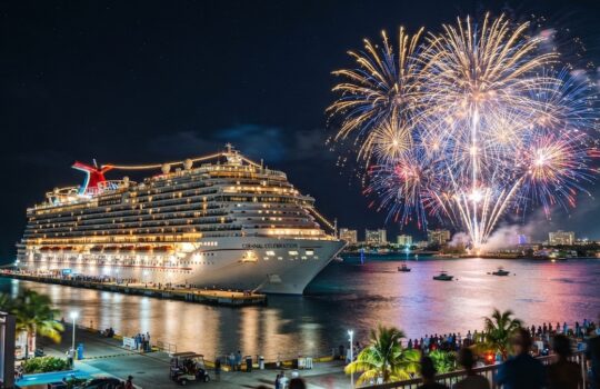 Large cruise ship docked at night with a vibrant fireworks display over the harbor behind it.