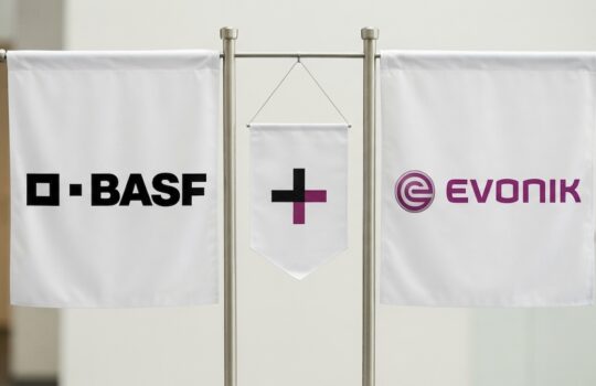 Three white banners on a metal stand displaying BASEF on the left, a central cross banner, and the Evonik logo on the right.