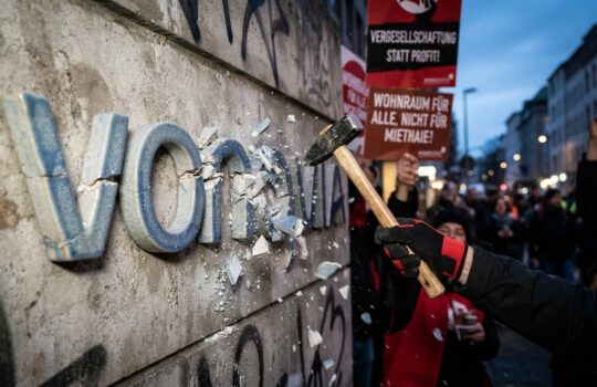 Close-up of a protester smashing a concrete wall with a hammer during a street demonstration.