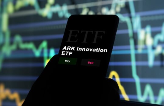 Smartphone screen displaying 'ARK Innovation ETF' with Buy and Sell buttons over a background of stock charts and data lines.