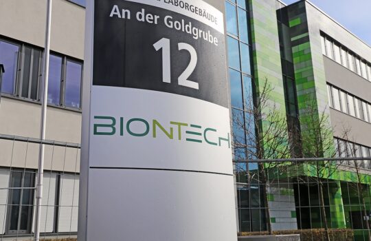 Sign at a modern building reading 'An der Goldgrube 12' with the BioNTech logo, in front of a glass-and-green facade exterior.