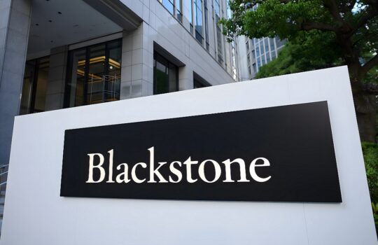 Blackstone sign on a white display panel outside a modern office building with trees nearby.