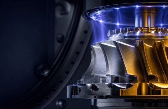 Close-up of a high-precision turbine rotor with silver and gold blades, illuminated by a blue glow inside a dark metal chamber