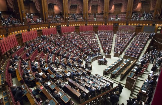 A large semicircular legislative chamber with rows of red seats and wooden desks