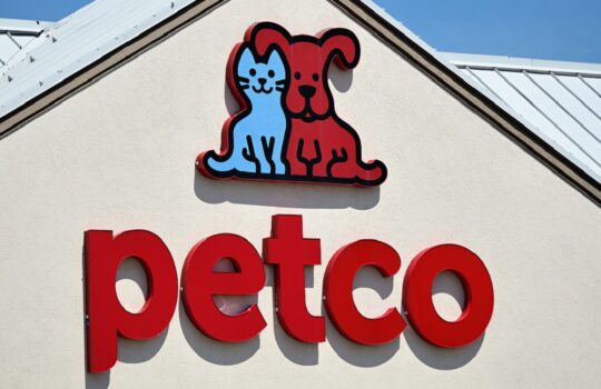 Petco storefront sign with blue cat and red dog logo above the red 'petco' lettering on a beige wall.