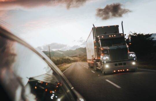 A semi truck driving on a highway under a warm orange sky