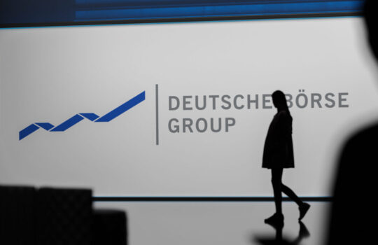 Deutsche Börse Group logo on a light panel with a blue line-graph motif and a dark- silhouetted figure walking by.