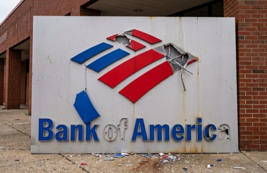 Damaged Bank of America sign outside a brick building with broken panels and debris on the ground.