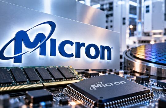 Micron logo on a metallic panel above circuit boards in a high-tech manufacturing setting.