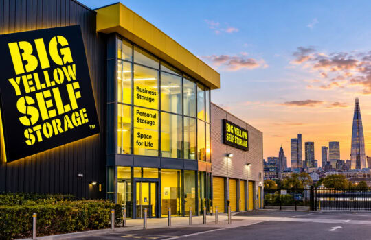 Exterior of Big Yellow Self Storage building at sunset, with large yellow-and-black sign and glass entrance.