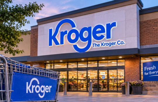 Kroger storefront at dusk with a large blue Kroger sign and shopping carts in the foreground